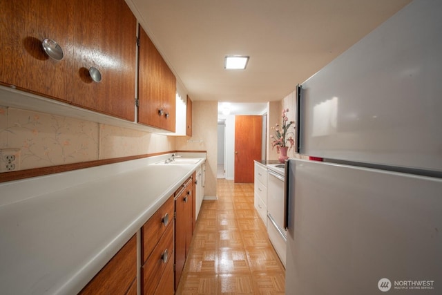kitchen with a sink, light countertops, brown cabinetry, and freestanding refrigerator