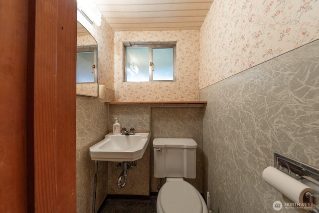 half bathroom featuring a sink, toilet, and wallpapered walls