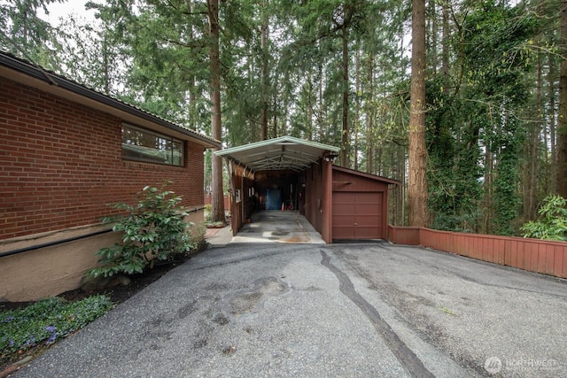 view of side of home with a carport, a garage, an outdoor structure, brick siding, and driveway
