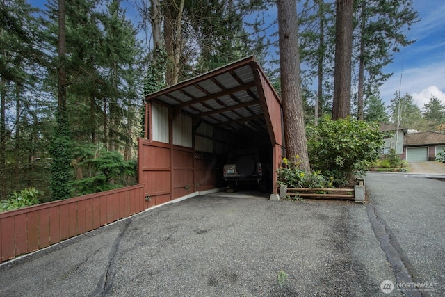 view of parking featuring aphalt driveway, a carport, and an outbuilding