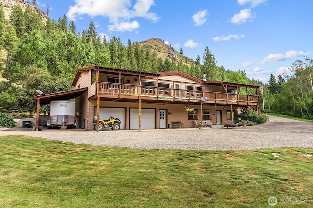 back of property featuring stairway, an attached garage, gravel driveway, a deck with mountain view, and a yard