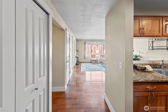hall with baseboards, wood finished floors, a sink, and a textured ceiling