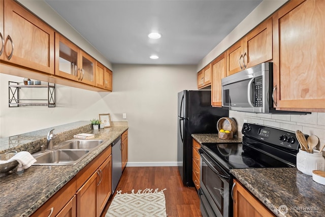 kitchen with appliances with stainless steel finishes, glass insert cabinets, a sink, dark wood-style floors, and backsplash