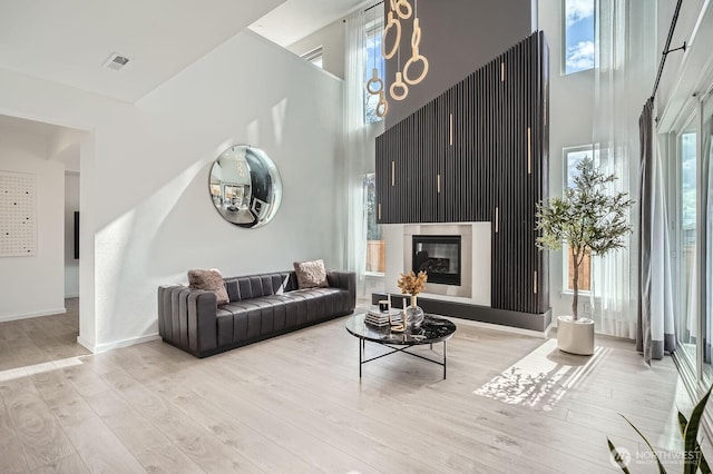 living room featuring a glass covered fireplace, a high ceiling, baseboards, and wood finished floors