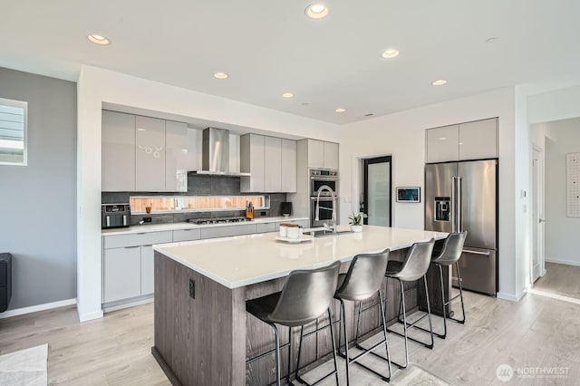 kitchen featuring gray cabinets, wall chimney range hood, modern cabinets, a breakfast bar area, and appliances with stainless steel finishes