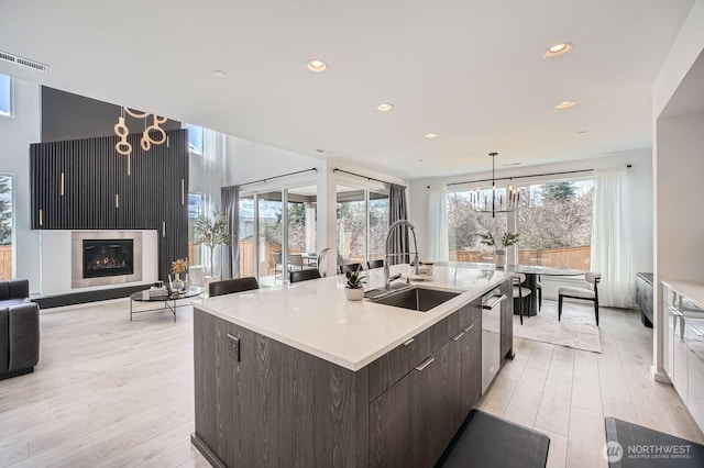 kitchen featuring a sink, dark brown cabinets, light wood-style floors, and a center island with sink