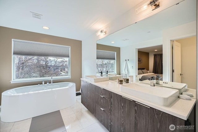 ensuite bathroom featuring a freestanding tub, a sink, double vanity, ensuite bath, and tile patterned flooring