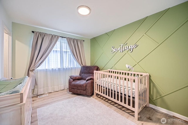 bedroom featuring a crib, visible vents, baseboards, and wood finished floors
