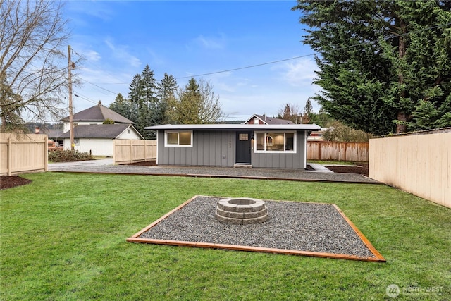 back of house featuring an outbuilding, a fenced backyard, board and batten siding, a fire pit, and a lawn