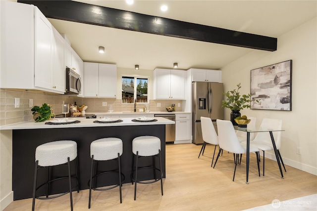 kitchen with beamed ceiling, a peninsula, appliances with stainless steel finishes, white cabinetry, and a kitchen breakfast bar