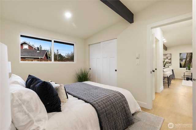 bedroom featuring light wood-style flooring, a closet, lofted ceiling with beams, and baseboards