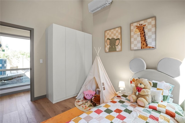 bedroom with an AC wall unit, wood finished floors, a high ceiling, and baseboards