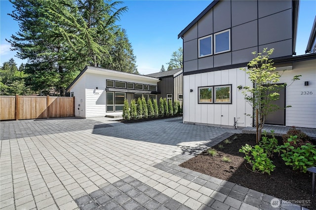rear view of house with board and batten siding, fence, and a patio