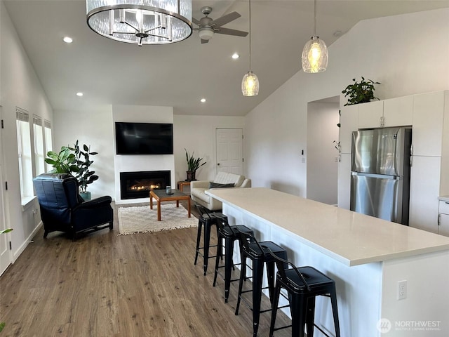 kitchen featuring light countertops, hanging light fixtures, freestanding refrigerator, a glass covered fireplace, and wood finished floors