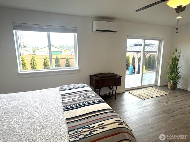 bedroom with a wall unit AC, baseboards, access to exterior, a ceiling fan, and wood finished floors