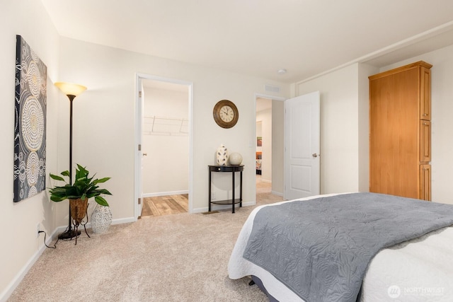bedroom featuring light colored carpet, baseboards, a walk in closet, and visible vents