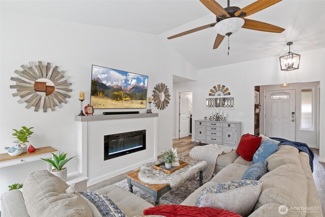living area featuring a glass covered fireplace, high vaulted ceiling, light wood-style floors, and a ceiling fan