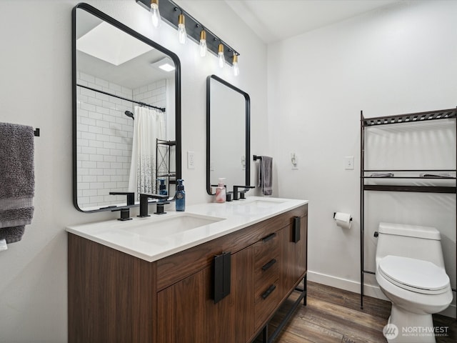 full bathroom with double vanity, a sink, toilet, and wood finished floors