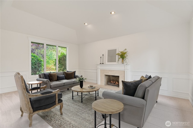 living area with a decorative wall, wainscoting, vaulted ceiling, a tile fireplace, and light colored carpet