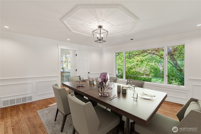 dining room with plenty of natural light, a decorative wall, crown molding, light wood-style floors, and a chandelier