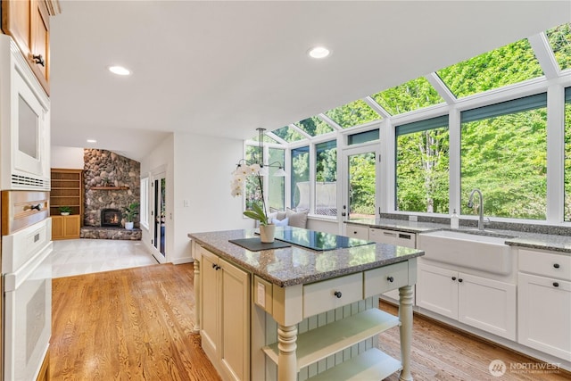 kitchen with a sink, vaulted ceiling, a fireplace, light stone counters, and recessed lighting
