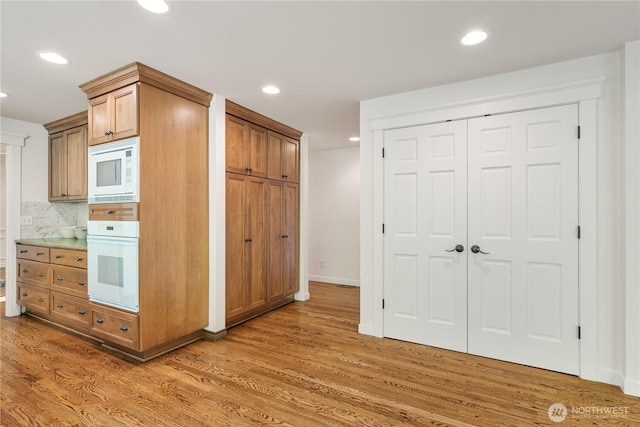 kitchen featuring white appliances, light wood-style flooring, recessed lighting, backsplash, and brown cabinets