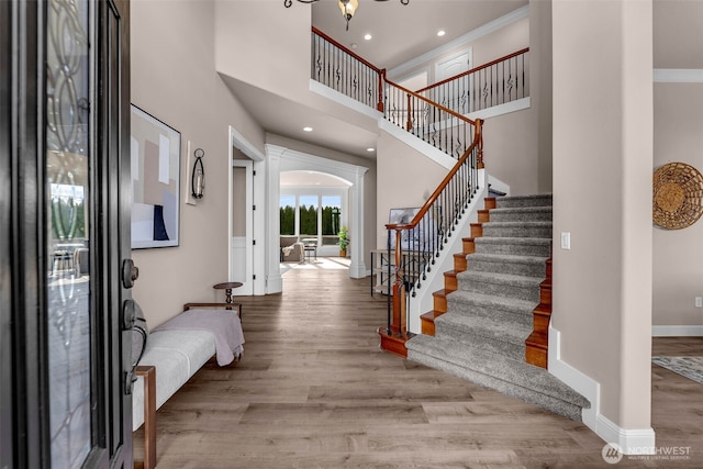 entryway with stairs, baseboards, a towering ceiling, arched walkways, and wood finished floors