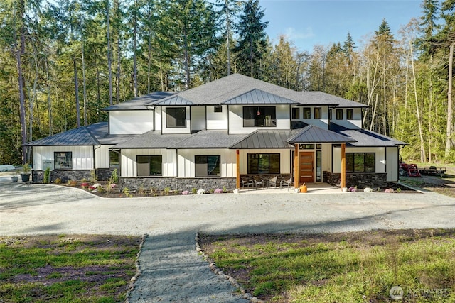 view of front of house featuring a standing seam roof, stone siding, board and batten siding, metal roof, and a forest view