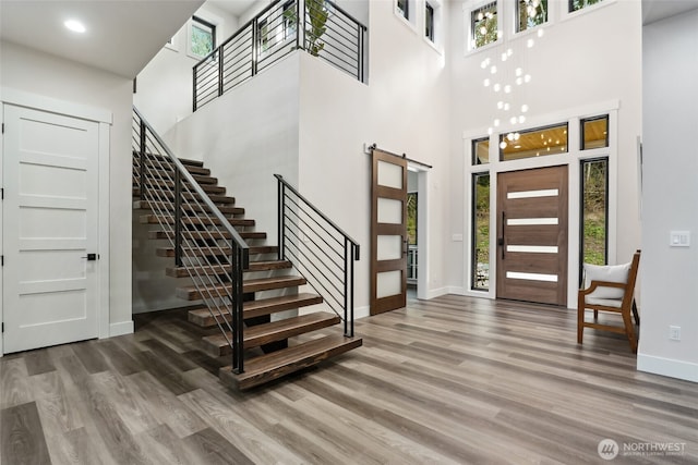 entryway featuring stairs, a high ceiling, a barn door, wood finished floors, and baseboards