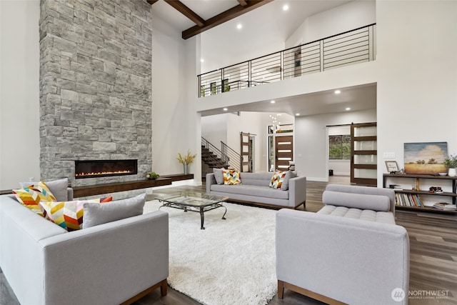 living room with stairway, baseboards, beam ceiling, a stone fireplace, and wood finished floors