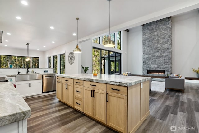 kitchen featuring stainless steel dishwasher, a stone fireplace, light brown cabinetry, and a sink