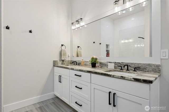 full bathroom with double vanity, a sink, baseboards, and a tile shower