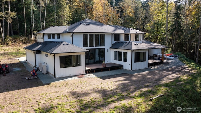 back of property with a forest view, roof with shingles, crawl space, and a deck