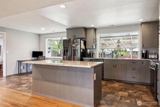 kitchen with light stone countertops, a sink, stainless steel appliances, recessed lighting, and a kitchen island