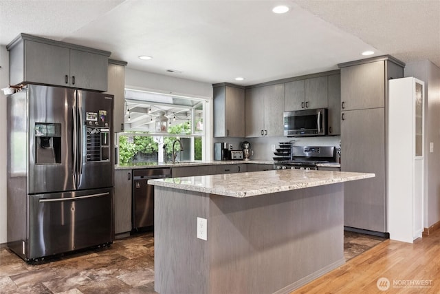 kitchen with light stone countertops, appliances with stainless steel finishes, a sink, a center island, and gray cabinetry