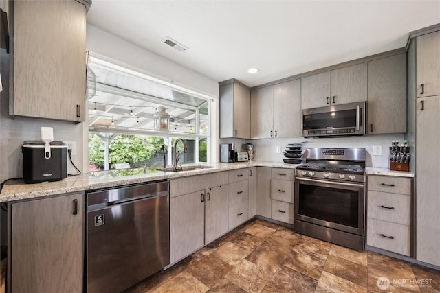 kitchen featuring visible vents, stone finish floor, a sink, gray cabinetry, and stainless steel appliances