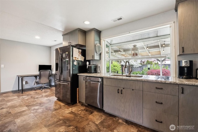 kitchen featuring light stone counters, a sink, dishwasher, refrigerator with ice dispenser, and visible vents