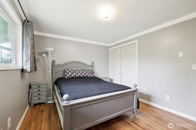 bedroom featuring crown molding, a textured ceiling, baseboards, wood finished floors, and a closet
