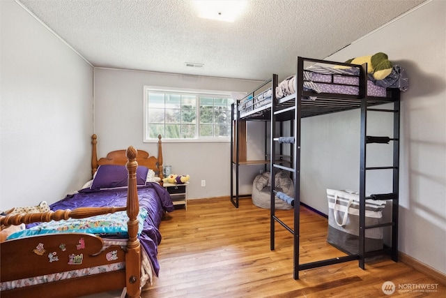 bedroom featuring visible vents, a textured ceiling, and wood finished floors