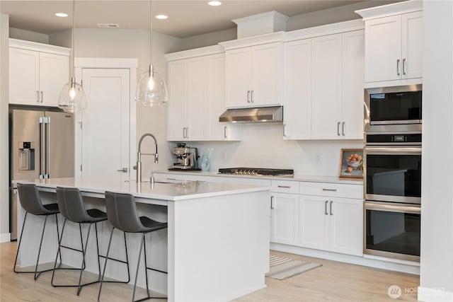 6346 Marymere Rd SW, Port Orchard, WA 98367 - kitchen with under cabinet range hood, appliances with stainless steel finishes, light wood-style floors, a kitchen island with sink, and recessed lighting