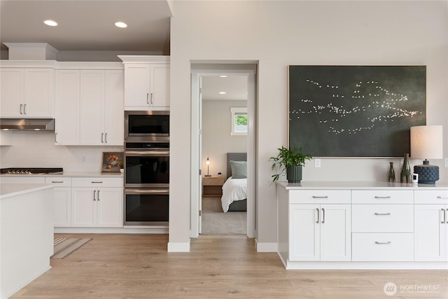 6346 Marymere Rd SW, Port Orchard, WA 98367 - kitchen featuring under cabinet range hood, appliances with stainless steel finishes, white cabinets, light wood-style flooring, and decorative backsplash