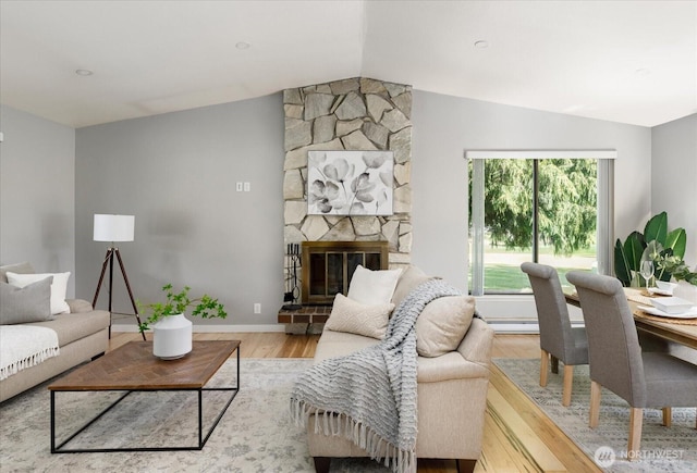 living room featuring a stone fireplace, baseboards, lofted ceiling, and wood finished floors