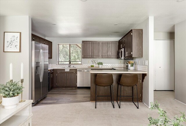 kitchen featuring light countertops, a peninsula, stainless steel appliances, dark brown cabinets, and a breakfast bar area