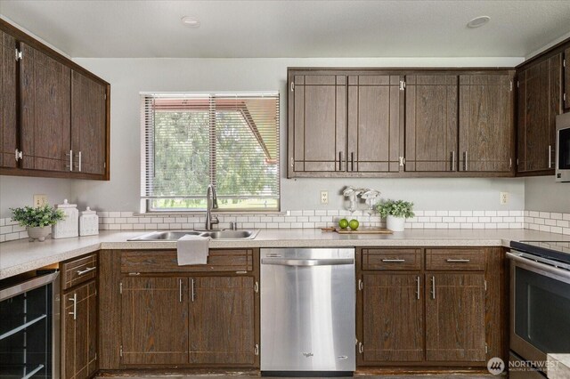 kitchen featuring light countertops, wine cooler, stainless steel appliances, dark brown cabinets, and a sink