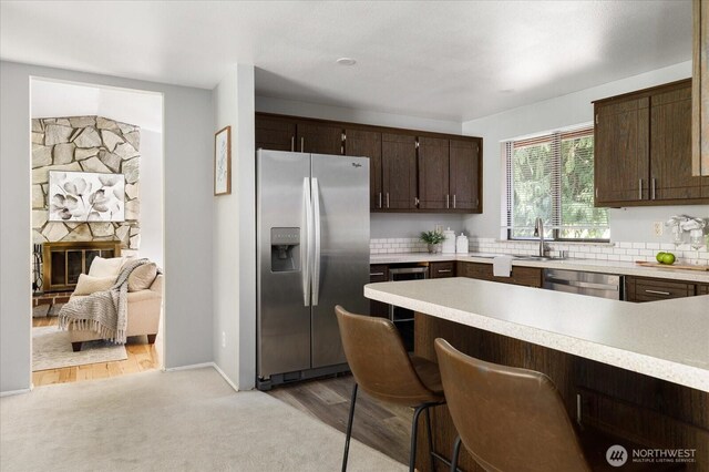 kitchen featuring light countertops, stainless steel appliances, dark brown cabinetry, a sink, and a breakfast bar area