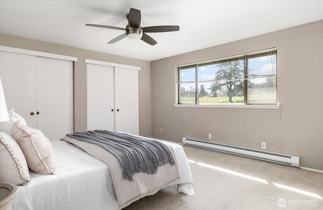 bedroom with a baseboard radiator, a ceiling fan, carpet, and two closets