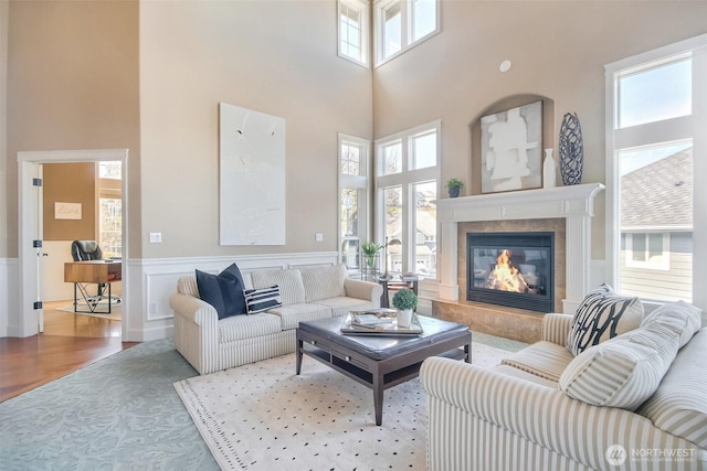 living area with wood finished floors, a towering ceiling, a wainscoted wall, and a fireplace