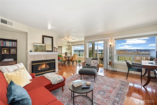 living area with visible vents, hardwood / wood-style flooring, baseboards, a fireplace, and a notable chandelier