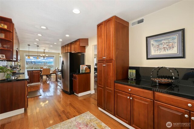 kitchen featuring open shelves, light wood-type flooring, dark countertops, visible vents, and freestanding refrigerator