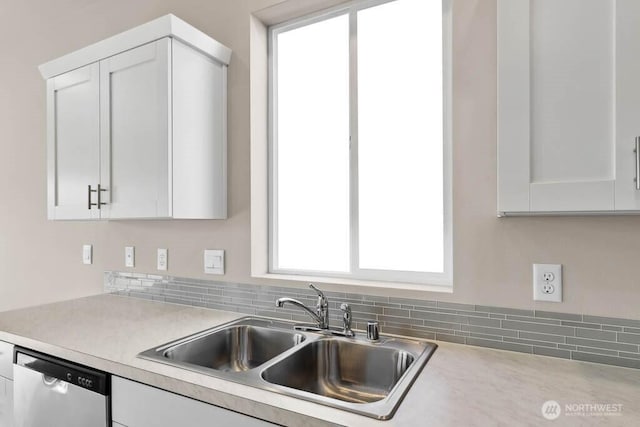 kitchen with stainless steel dishwasher, white cabinetry, light countertops, and a sink